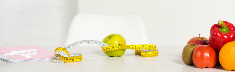 panoramic shot of fresh fruits and vegetables, measure tape and textbook on table