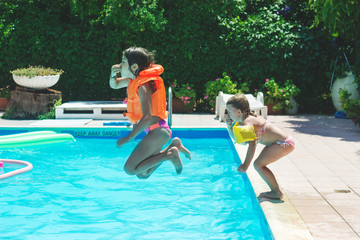 Two little girls enjoys summer, jumping in the water on the pool