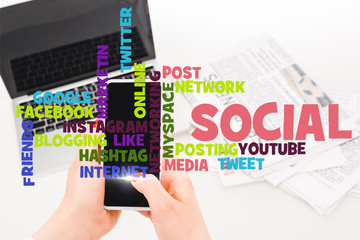 selective focus of woman holding smartphone near laptop and newspapers with social media illustration