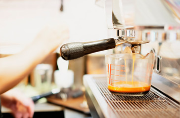 In the coffee shop, barista is making espresso, pouring coffee in the measuring cup. Blurry background.