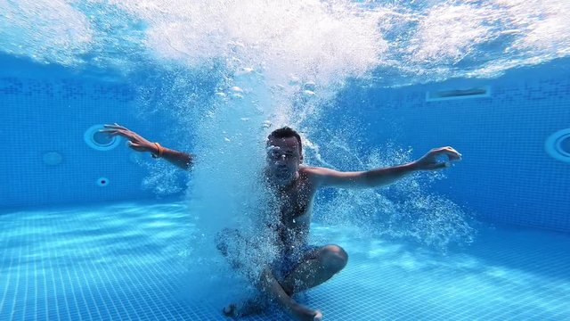 Man jumps into clear water of a pool in yoga pose. Underwater camera shooting a video of a man jumping into water. Male shows gesture yes with thumbs underwater.