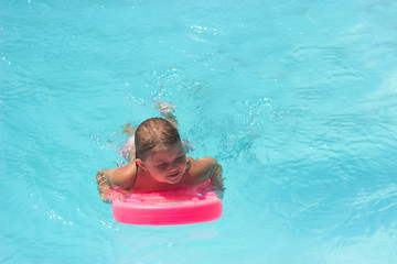 Little girl on the floating board, learns to swim in the pool