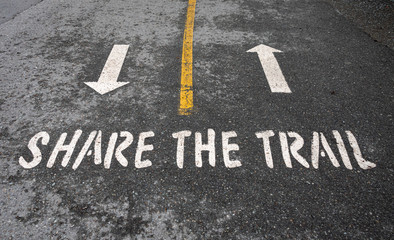 Share the Trail sign stenciled on an asphalt trail with directional arrows and yellow dividing line