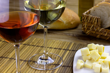 glass of white wine and glass of rose wine on wooden table with bread basket, cheese board and olive oil