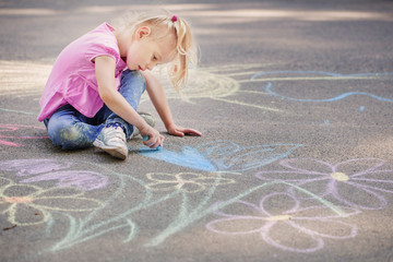 little girl draws with chalk on  pavement