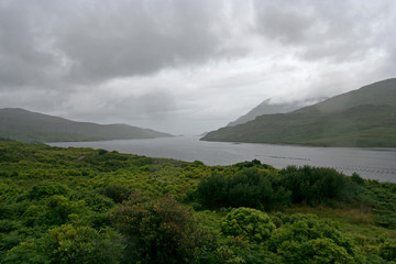 The bay with green mountainous coasts on the cloudy windy cold day