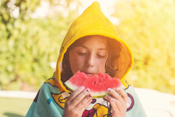 Close up of a little girl in her beach towel, eating watermelon on the poolside