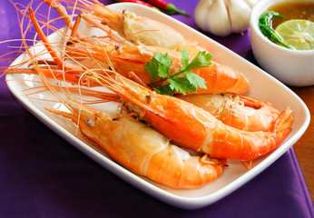 Cooked prawns or river shrimp on white plate with mixed chilli seafood sauce and violet silk background.