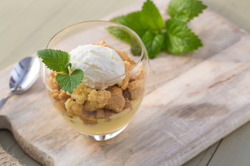 Apple crumble topping vanilla ice cream served with melisa in glass and wooden tray on table.