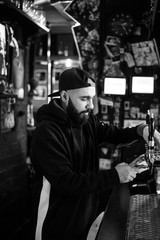 smiling barman pouring beer in a bar. Bearded courageous man pours you a foaming drink. Black and white photo