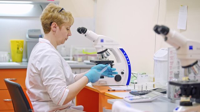 Woman researcher works with a microscope in a lab. Woman scientist prepares microscope for doing a research. Science laboratory research.