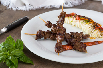 Asian style grilled teriyaki beef skewers on a white plate, top view. Delicious appetizer