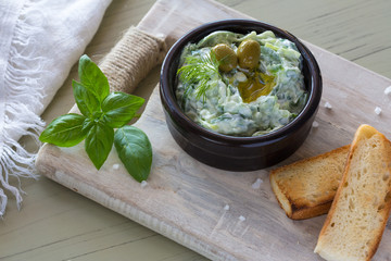 Greek dip sauce or dressing tzatziki and ingredients decorated with olive oil and basil on wooden table