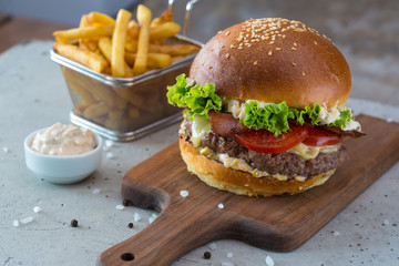 Highigh burger with french fries in small fry basket on concrete surface. Traditional American fastfood.
