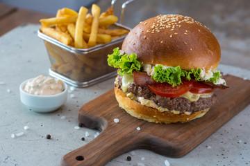 Highigh burger with french fries in small fry basket on concrete surface. Traditional American fastfood.