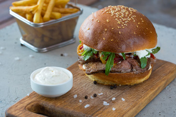 Highigh burger with french fries in small fry basket on concrete surface. Traditional American fastfood.