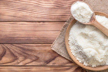 Wooden bowl and wooden spoon with grated parmesan on wooden background. Top view. Space for text.
