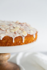 almond olive oil cake with brown butter icing and sliced almonds, dripping icing on cake, marble and wood cake stand, styled bakery