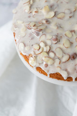 almond olive oil cake with brown butter icing and sliced almonds, dripping icing on cake, marble and wood cake stand, styled bakery