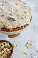 Fototapeta na wymiar almond olive oil cake with brown butter icing and sliced almonds, dripping icing on cake, marble and wood cake stand, styled bakery