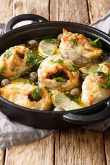 Greek cuisine cod steaks with lemon and olives closeup in a pan. vertical