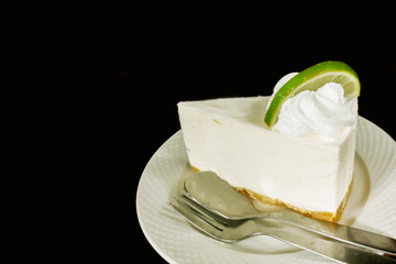 Thai style lime cream cake with teaspoon and fork on white ceramic plate and isolated on black background.