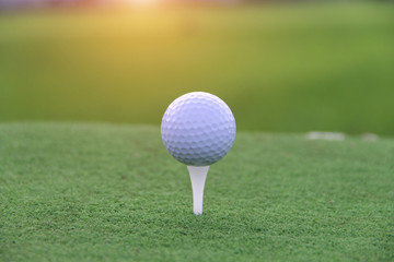 Golf ball on tee in beautiful golf course at sunset background.