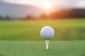 Golf ball on tee in beautiful golf course at sunset background.