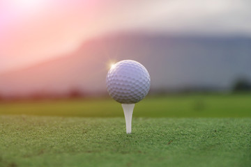 Golf ball on tee in beautiful golf course at sunset background.