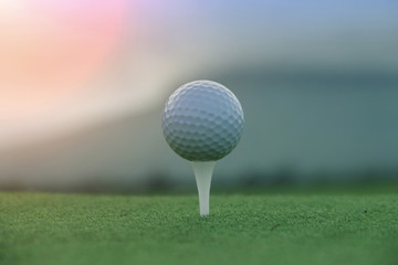 Golf ball on tee in beautiful golf course at sunset background.