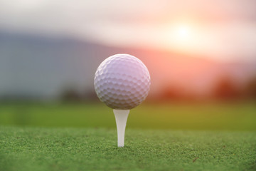 Golf ball on tee in beautiful golf course at sunset background.
