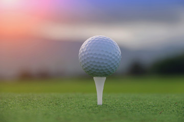 Golf ball on tee in beautiful golf course at sunset background.