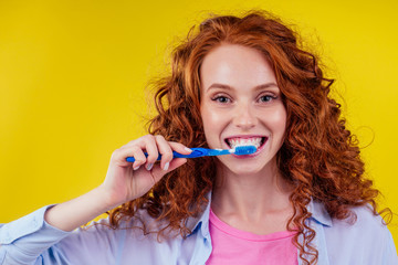 redhaired ginger woman brushing teeth with toothpaste eco paste on yellow studio background