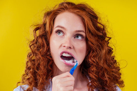 sleepy redhaired ginger woman brushing teeth with toothpaste eco paste on yellow studio background