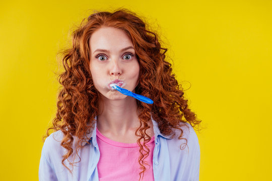 sleepy redhaired ginger woman brushing teeth with toothpaste eco paste on yellow studio background