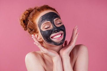 redhaired ginger young caucasian woman with natural anti acne mask on her pretty perfect face in studio pink background