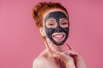 redhaired ginger young caucasian woman with natural anti acne mask on her pretty perfect face in studio pink background