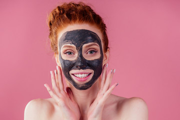 redhaired ginger young caucasian woman with natural anti acne mask on her pretty perfect face in studio pink background