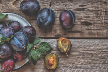 Fresh pile of plums in a old bowl on rustic table with green leaf. Toned image. Soft focus. Copy space.