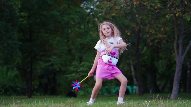 Girl with colorful pinwheel toy outdoors. Happy dancing little girl having fun with pinwheel
