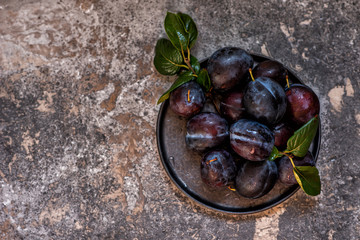 Fresh plum fruit with green leaf and water drops on grey background. Top view with copy space.