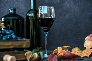 Red wine with bottle, glass and grapes on wooden background. Wine header image. Wineglass. Display in a winery or tavern of red grapes in a wooden box. Concept of the grape harvest, wine making.