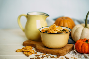 Pumpkin soup in a bowl with croutons and pumpkin seeds. Autumn food. Autumn seasonal cooking concept. Various autumn seasonal organic vegetables: pumpkin, carrot, paprika on wooden kitchen table.