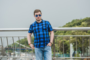 Portrait of young modern handsome man in blue plaid shirt and jeans at the city. Citizen lifestyle 