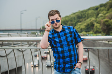 Portrait of young modern handsome man in blue plaid shirt and jeans at the city. Citizen lifestyle 