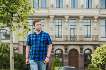 Portrait of young modern handsome man in blue plaid shirt and jeans at the city. Citizen lifestyle 