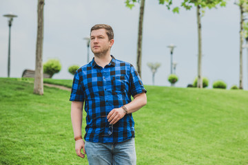 Portrait of young modern handsome man in blue plaid shirt and jeans at the city. Citizen lifestyle 