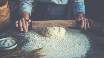 Homemade raw pastry on a wooden table on a rustic wooden surface with a rolling pin, flour, butter, wheat spikelets.