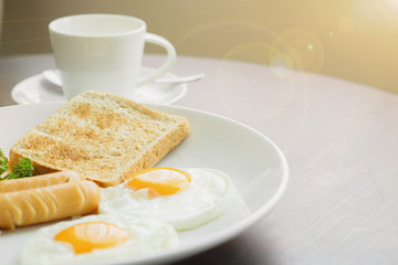 American breakfast and hot coffee in a white ceramic coffee cup on a wooden table with warm morning sunshine and lens flare background.