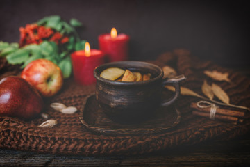 Fall leaves, hot cup of tea, knitted blanket, red berries, candles on wooden table background. Seasonal, autumnal hot drink. Autumn relaxing and still life concept. Toned image. Selective focus.